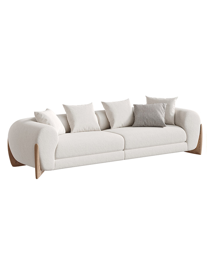 A modern luxury sofa with soft curved design, upholstered in elegant fabric with wooden side accents, EVOCA Sofa by INSIDE HOME.
